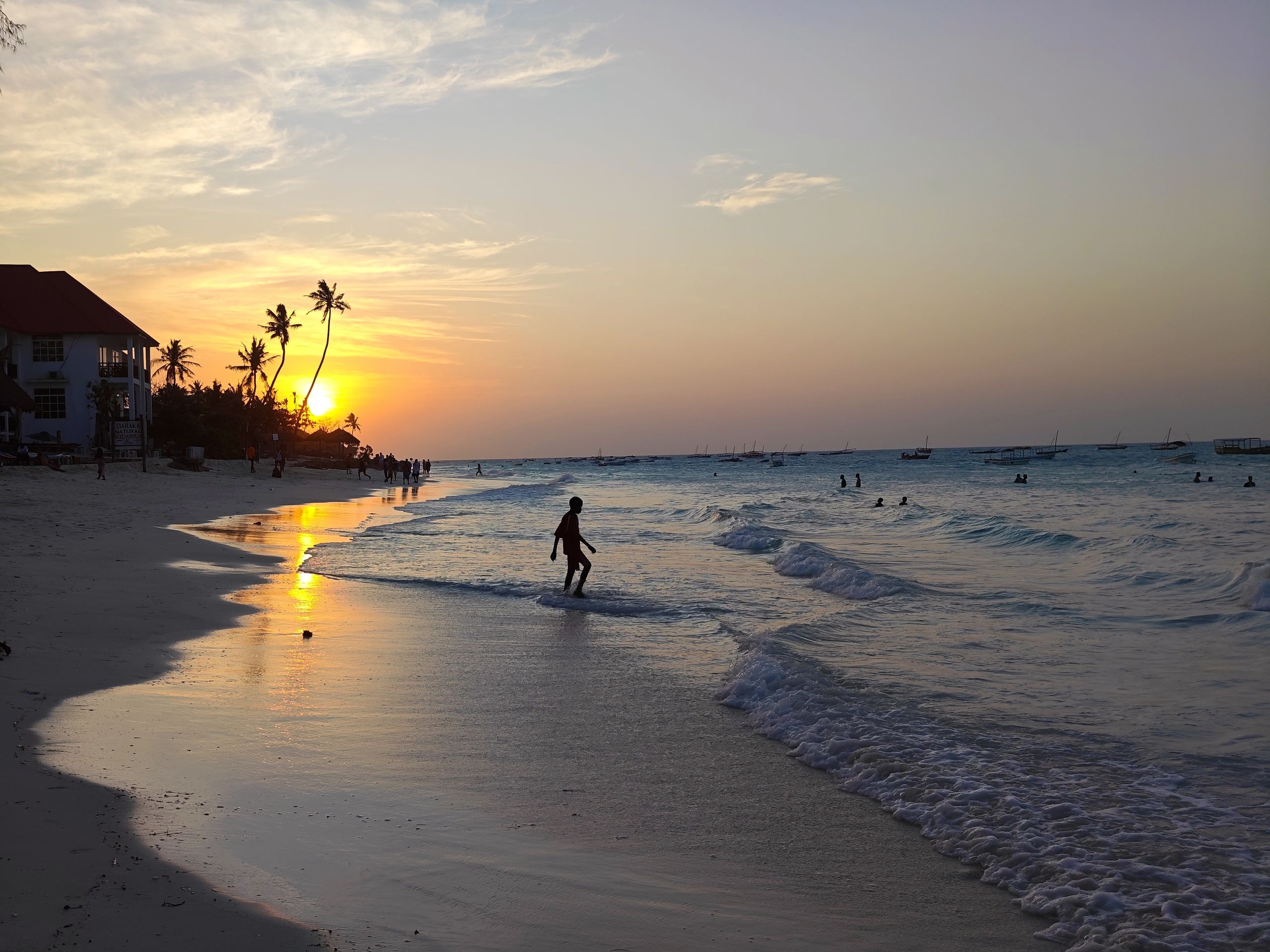 A tranquil beach at sunset featuring silhouettes of people along the shore.