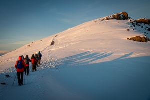 A group of hikers trekking a snowy mountain path at sunrise.