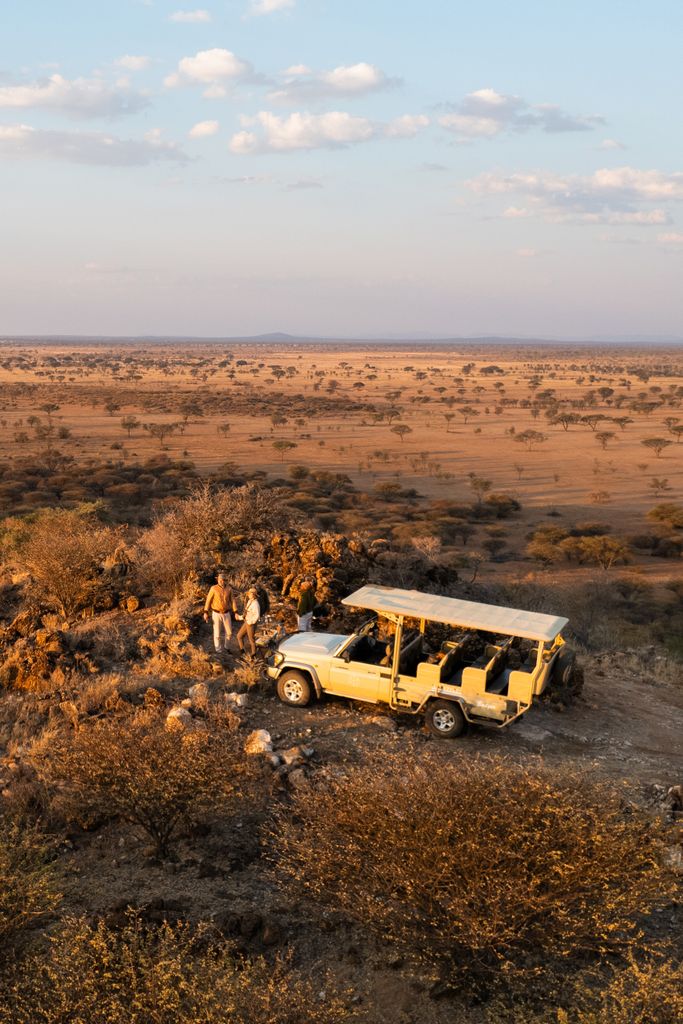 A safari jeep with two people in the African Savannah at sunset.