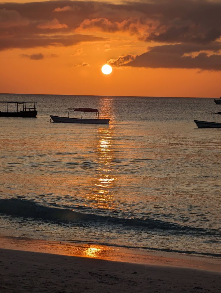 Beautiful sunset over a calm beach in Zanzibar, Tanzania with boats silhouetted against the orange sky.
