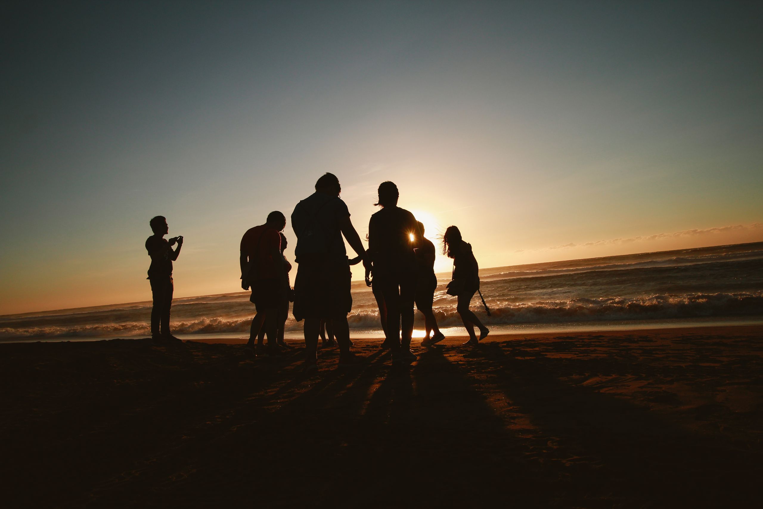 Silhouetted group of friends enjoying a scenic sunset on a sandy beach.