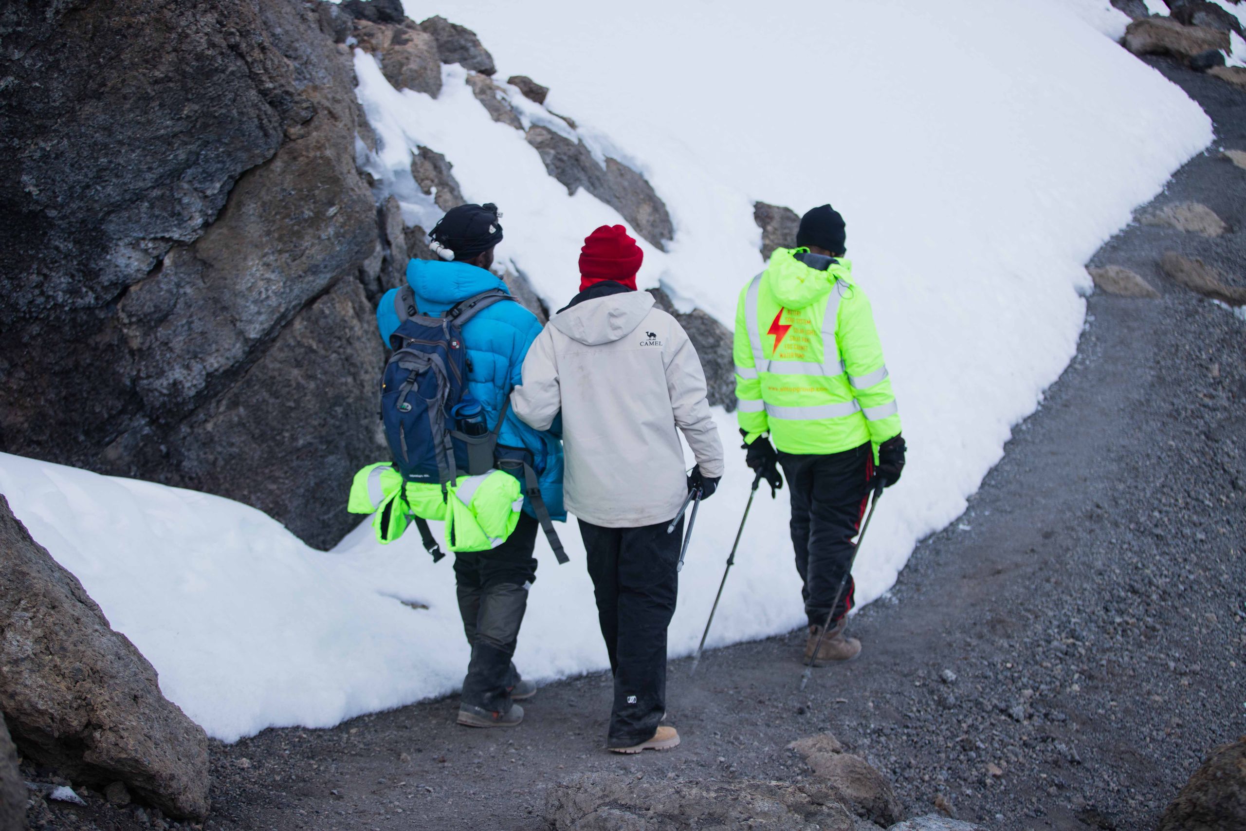 Three hikers navigate a snowy mountain trail, equipped with winter gear.